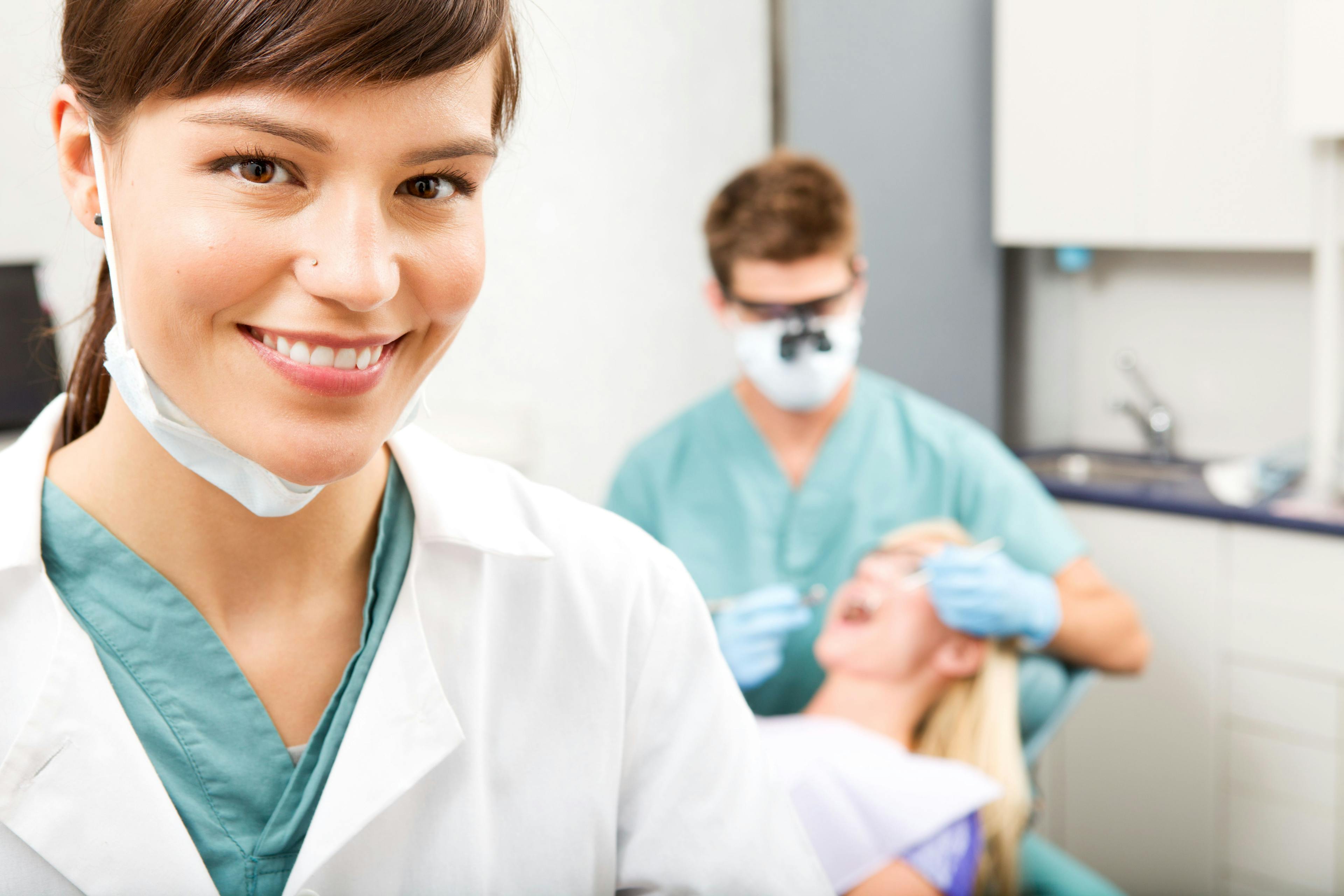 A dental hygienist smiles happily as the dentist checks the patient