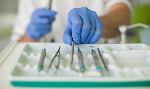 A gloved hand organizes dental instruments on a tray 