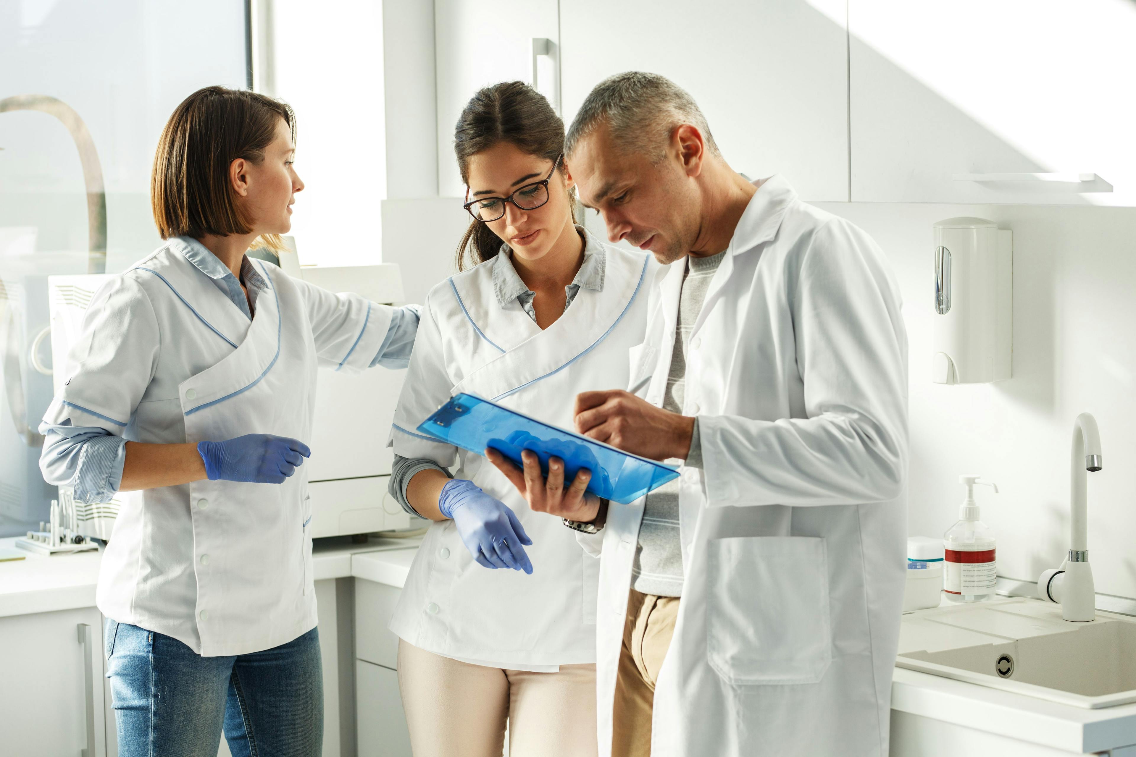 3 dental professionals in a dental office discuss something on a clipboard